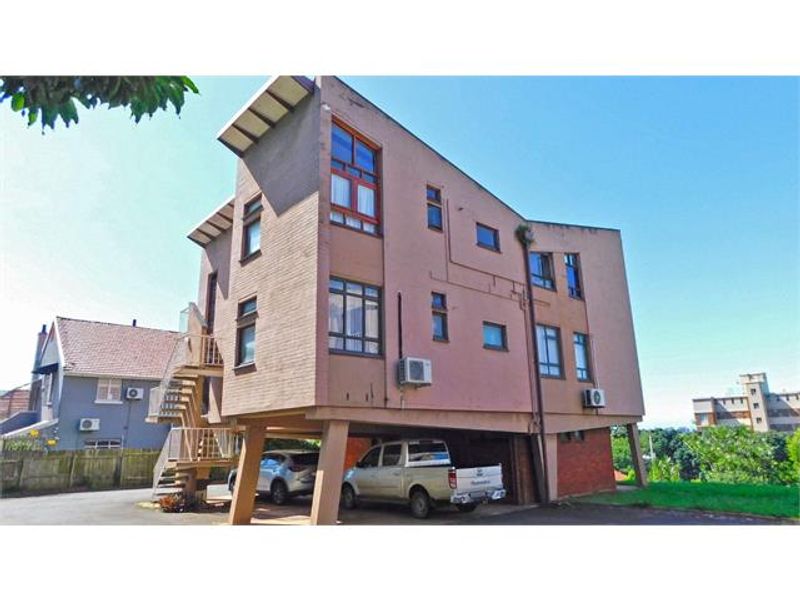 Exterior view of a multi-story apartment building featuring a stilt-supported ground level, external staircase, and brick facade with multiple window configurations.
