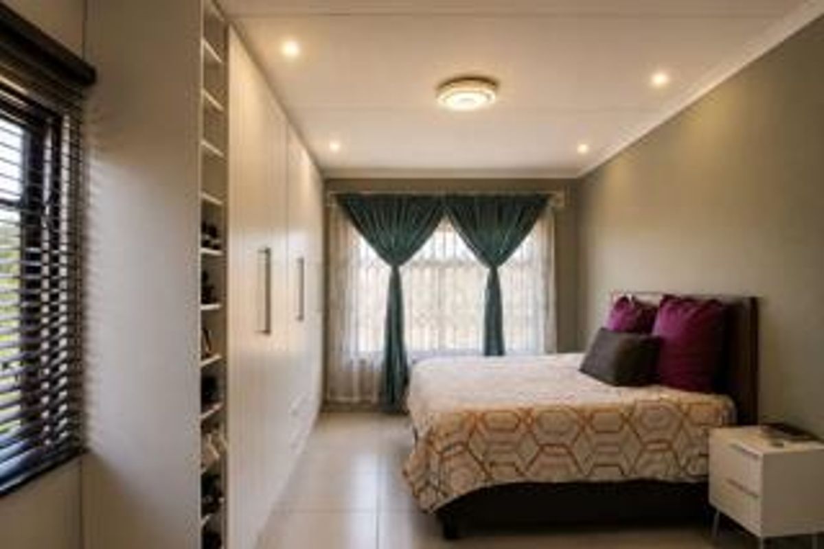 A well-maintained bedroom featuring extensive built-in cupboards, tiled flooring, recessed lighting, and large windows with venetian blinds.