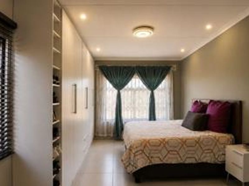 A well-maintained bedroom featuring extensive built-in cupboards, tiled flooring, recessed lighting, and large windows with venetian blinds.