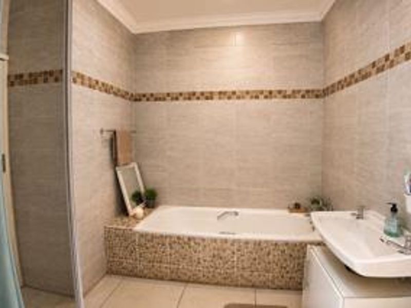 A functional bathroom featuring a built-in bathtub, wall-mounted basin, and tiled finishes throughout, including a separate shower enclosure.