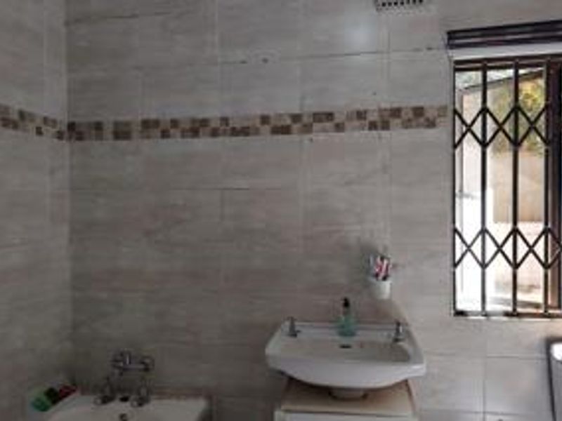 A functional bathroom featuring tiled walls, a wall-mounted basin, and a window fitted with a security gate.