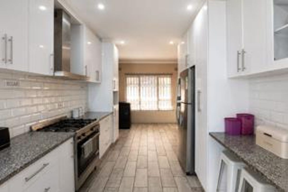 Modern galley-style kitchen featuring white cabinetry, granite countertops, subway tile backsplash, and stainless steel appliances with recessed lighting.