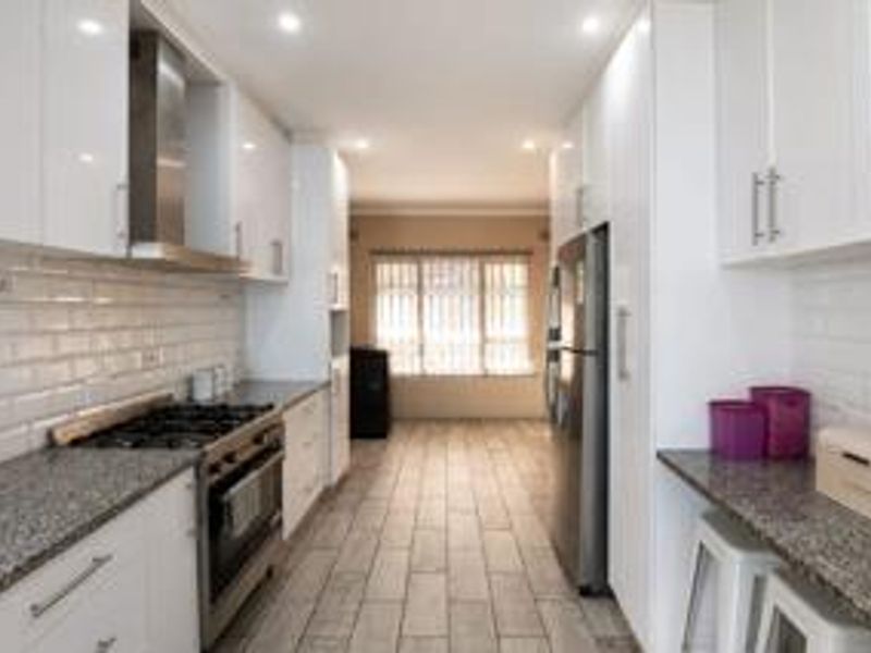 Modern galley-style kitchen featuring white cabinetry, granite countertops, subway tile backsplash, and stainless steel appliances with recessed lighting.