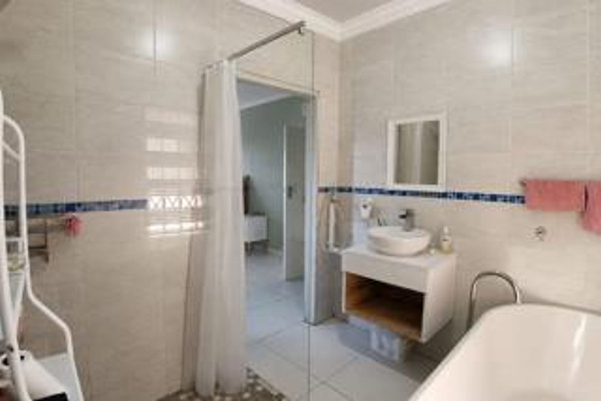 A modern bathroom featuring a wall-mounted vanity with a vessel sink, a freestanding bathtub, and a glass shower screen with tiled finishes.