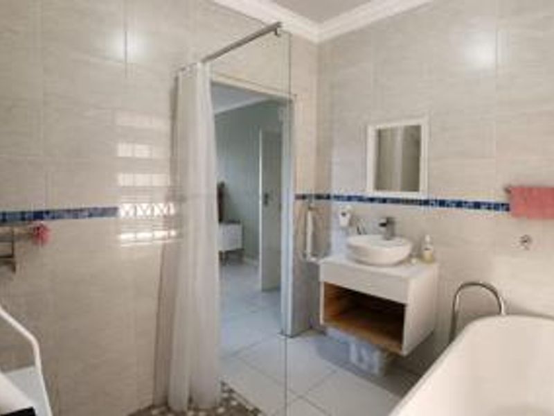A modern bathroom featuring a wall-mounted vanity with a vessel sink, a freestanding bathtub, and a glass shower screen with tiled finishes.