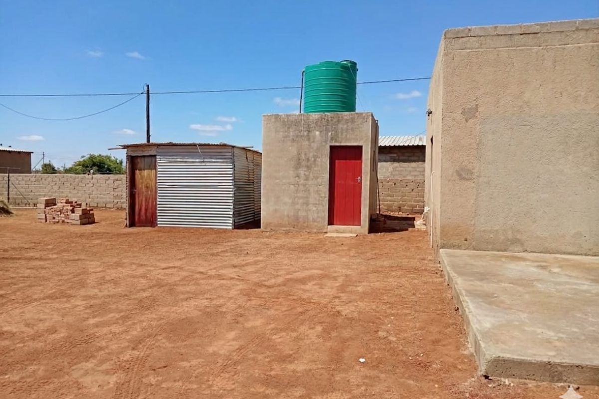 Rear exterior view showing a concrete masonry structure with a water tank, a corrugated metal shed, and an unpaved yard area.