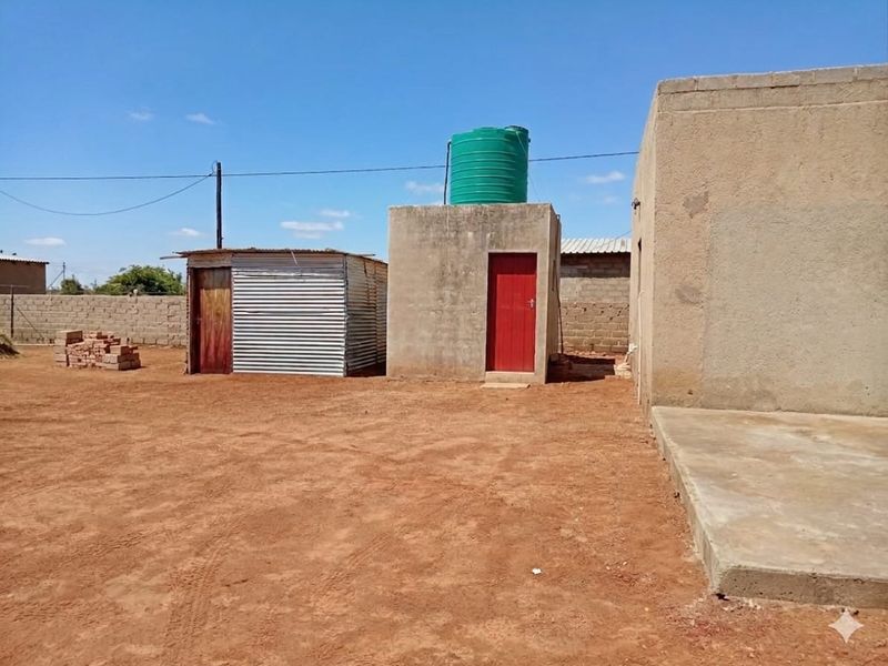 Rear exterior view showing a concrete masonry structure with a water tank, a corrugated metal shed, and an unpaved yard area.