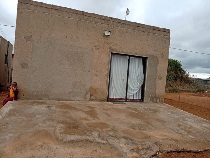 Rear exterior view of the property featuring a concrete patio area and a sliding glass door entrance with weathered wall finishes.