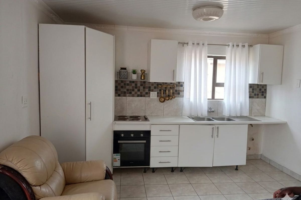 Open plan kitchen area featuring white cabinetry, built-in oven and hob, tiled backsplash, and double sink with tiled flooring.