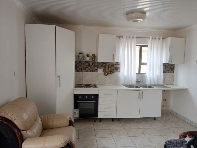 Open plan kitchen area featuring white cabinetry, built-in oven and hob, tiled backsplash, and double sink with tiled flooring.