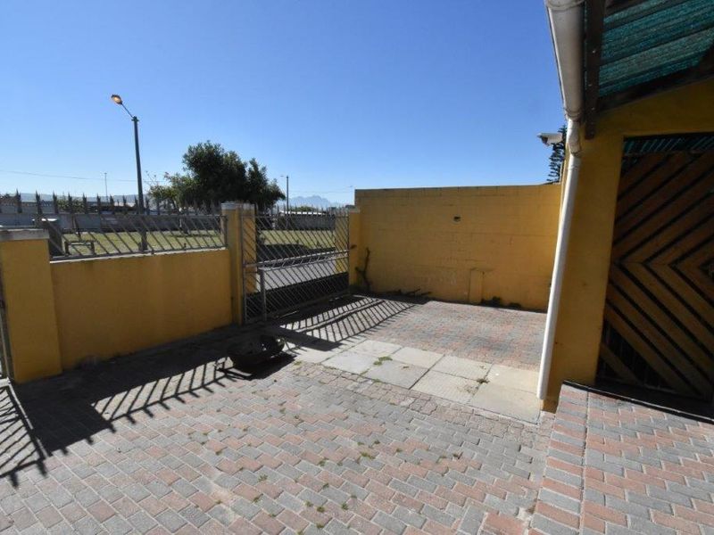 Front exterior area featuring a paved driveway, boundary wall with metal security gate, and integrated security camera.