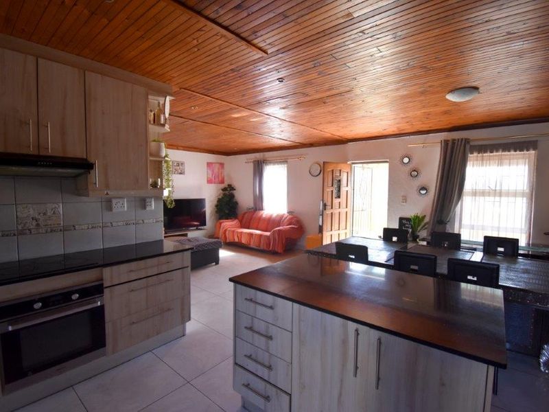 Open-plan living area featuring a functional kitchen with island, tiled floors, and a distinctive timber-clad ceiling, creating a warm and connected living space.