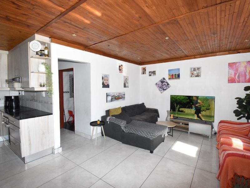 Open-plan living area featuring a timber-clad ceiling, tiled flooring, and a compact kitchen with built-in cabinetry and granite countertops.