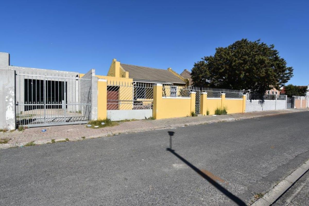Front street view of a residential property featuring a yellow boundary wall, metal security gate, and tiled roof structure.