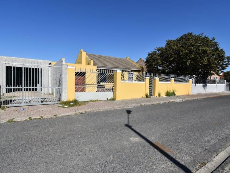 Front street view of a residential property featuring a yellow boundary wall, metal security gate, and tiled roof structure.