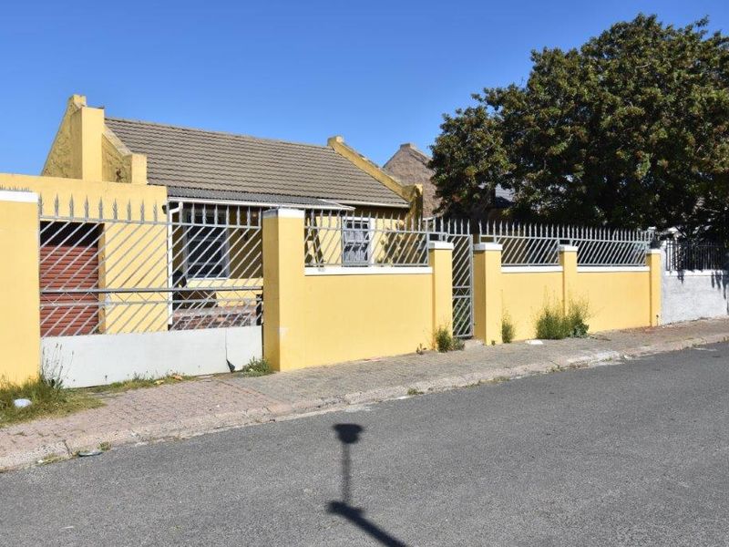 Front exterior view of a single-story house featuring a yellow perimeter wall, metal security fencing, and a tiled roof.