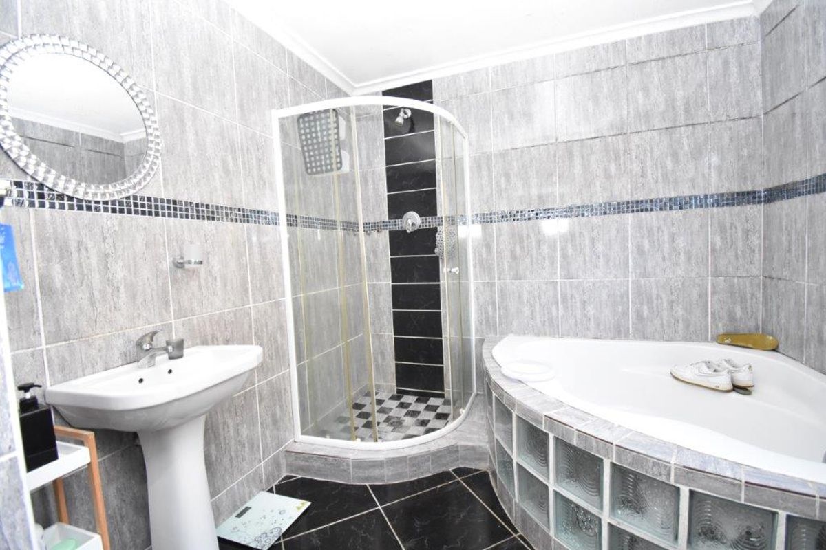 A functional bathroom featuring a corner shower enclosure, a corner bathtub with glass block detailing, and a pedestal basin with grey tiled finishes.