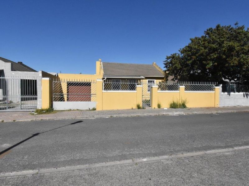 Front elevation of a single-story house featuring a yellow boundary wall with security spikes, a garage, and a tiled roof.