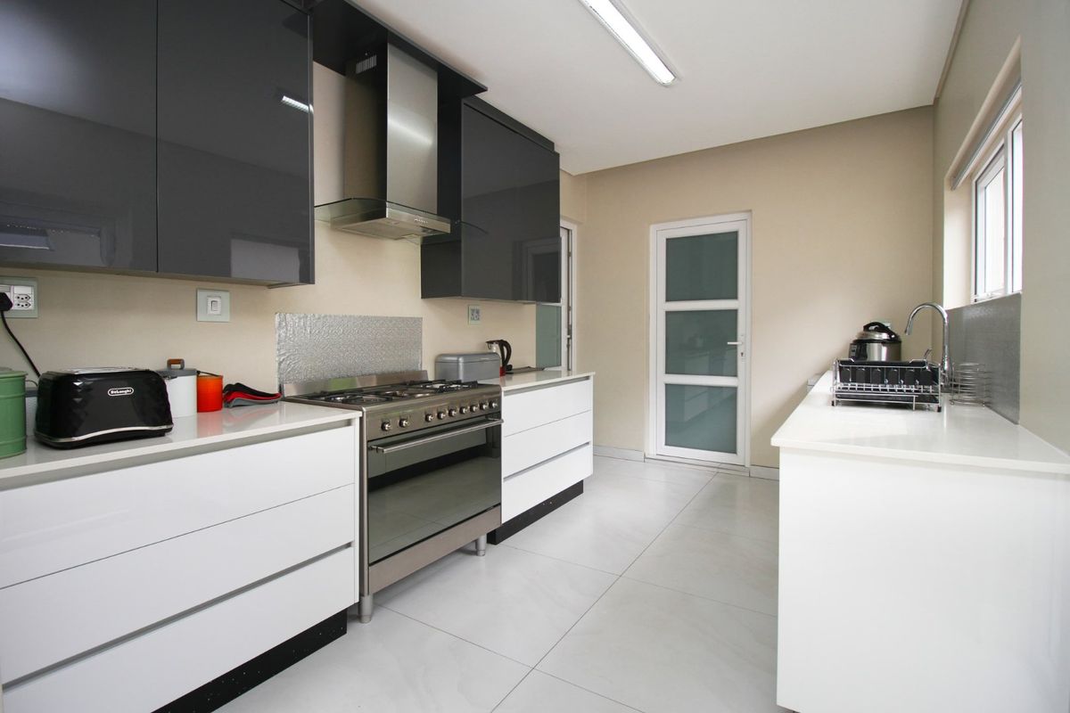 Modern kitchen featuring high-gloss cabinetry, stainless steel gas stove with extractor, quartz countertops, and tiled flooring with a functional layout.
