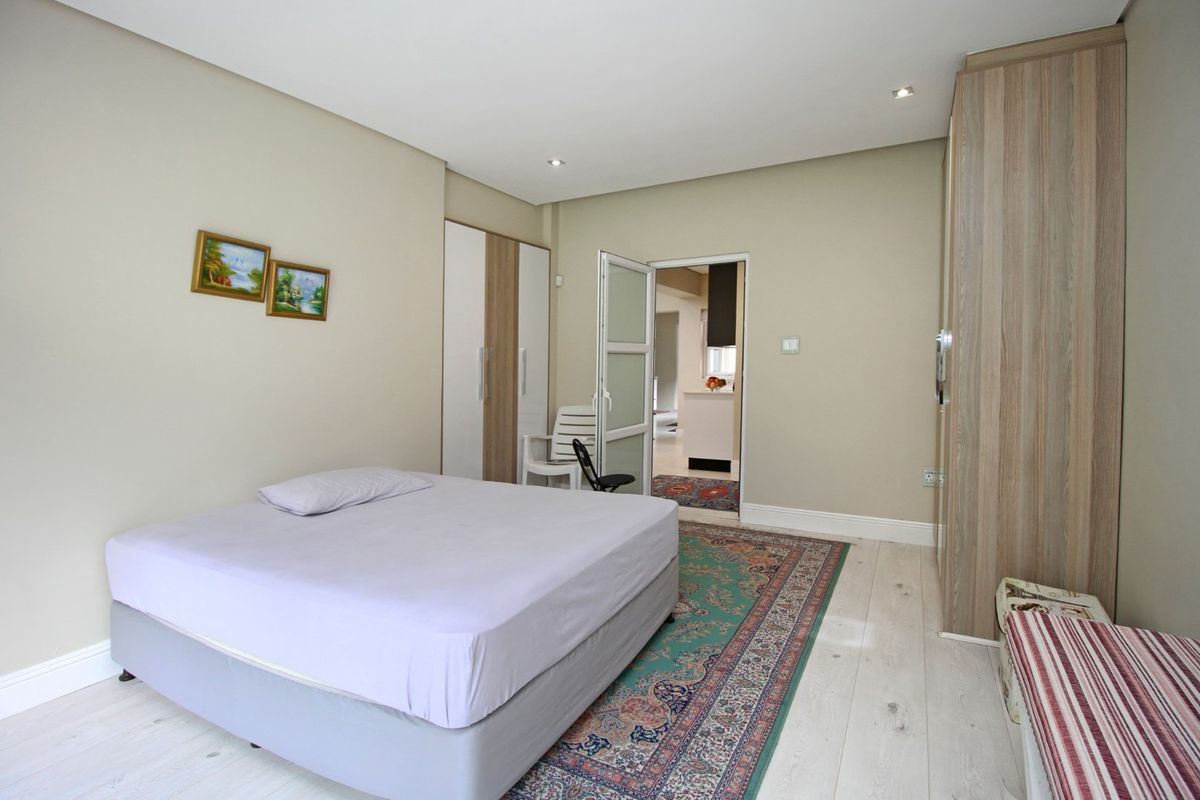 A well-maintained bedroom featuring built-in wardrobes, recessed lighting, and light-toned flooring, with direct access to an adjacent living area.