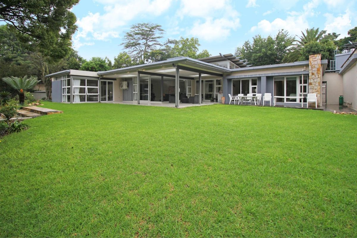 Spacious rear garden featuring a large manicured lawn and a covered patio area with sliding glass doors and stone-clad architectural detailing.