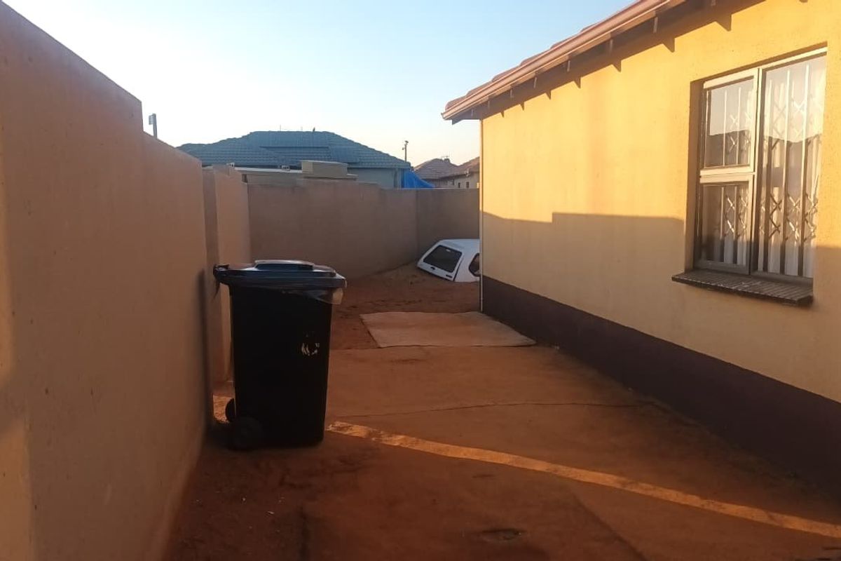 A view of the rear exterior area of the house, featuring a perimeter wall and a side window with security bars.