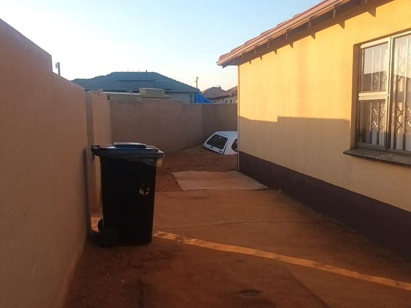 A view of the rear exterior area of the house, featuring a perimeter wall and a side window with security bars.