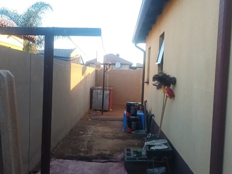 A narrow rear exterior side yard featuring a boundary wall, washing line, and basic utility space along the side of the house.