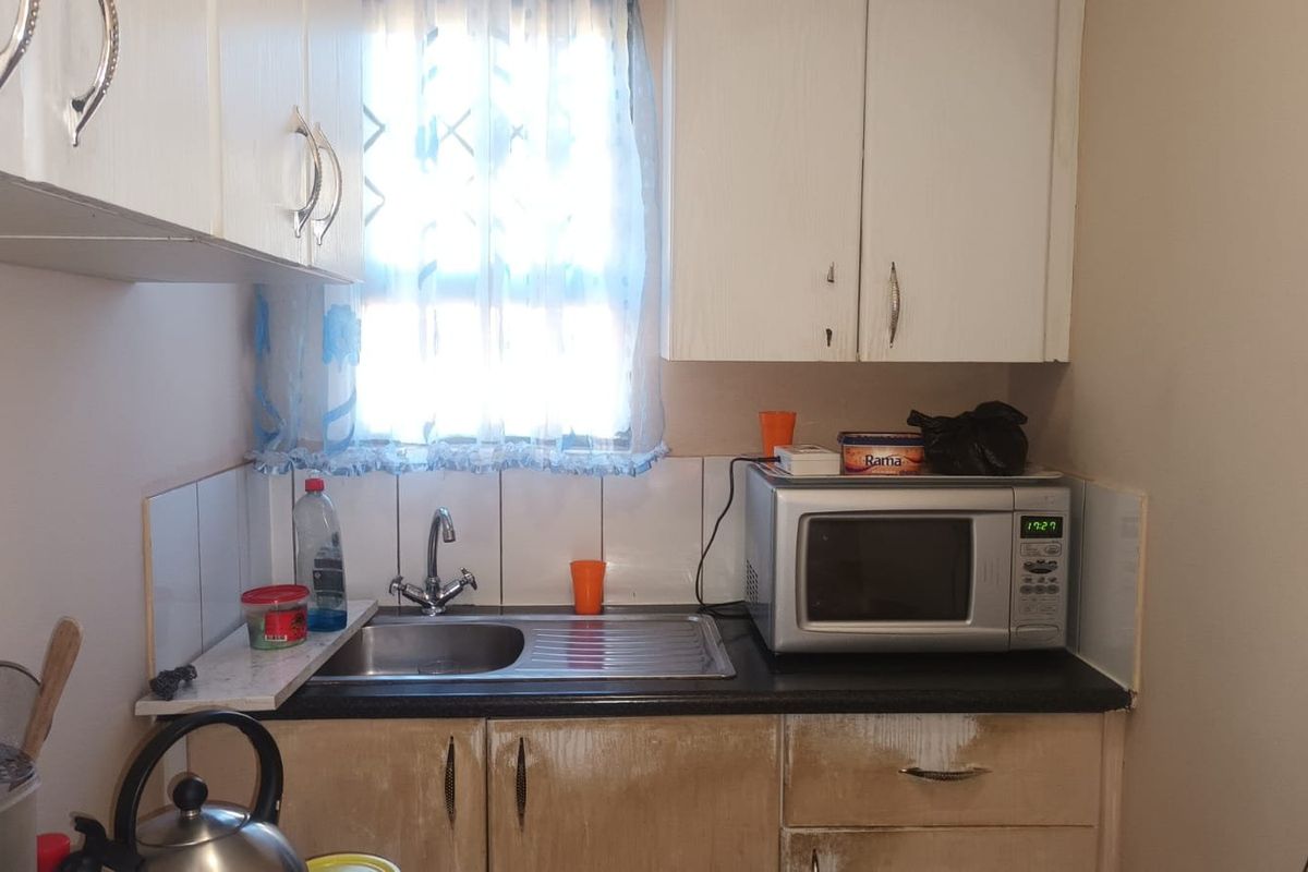 Compact kitchen area featuring built-in cabinetry, a stainless steel sink, and tiled splashback, showing signs of wear on the lower cabinet finishes.