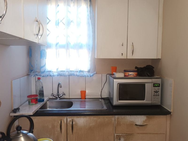 Compact kitchen area featuring built-in cabinetry, a stainless steel sink, and tiled splashback, showing signs of wear on the lower cabinet finishes.