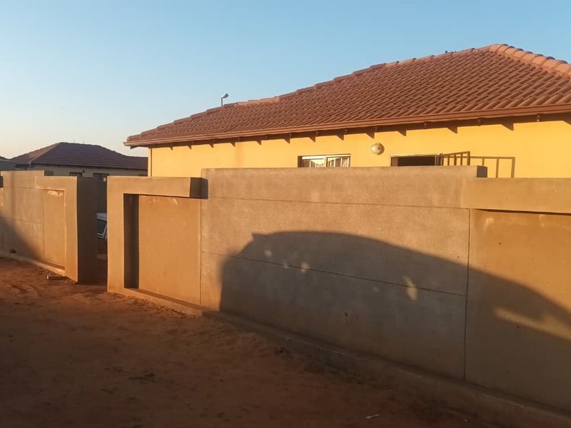 Front view of a single-story house featuring a tiled roof, plastered exterior walls, and a modern concrete boundary wall with a security gate.