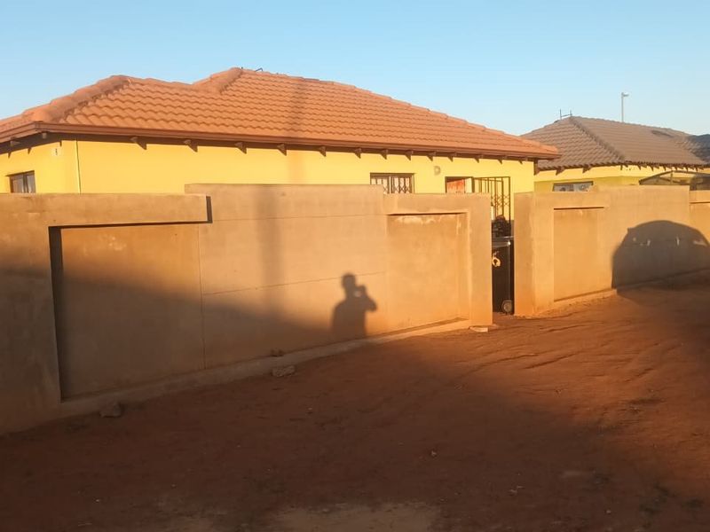 Front view of a residential house featuring a tiled roof and a concrete perimeter wall with a security gate entrance.