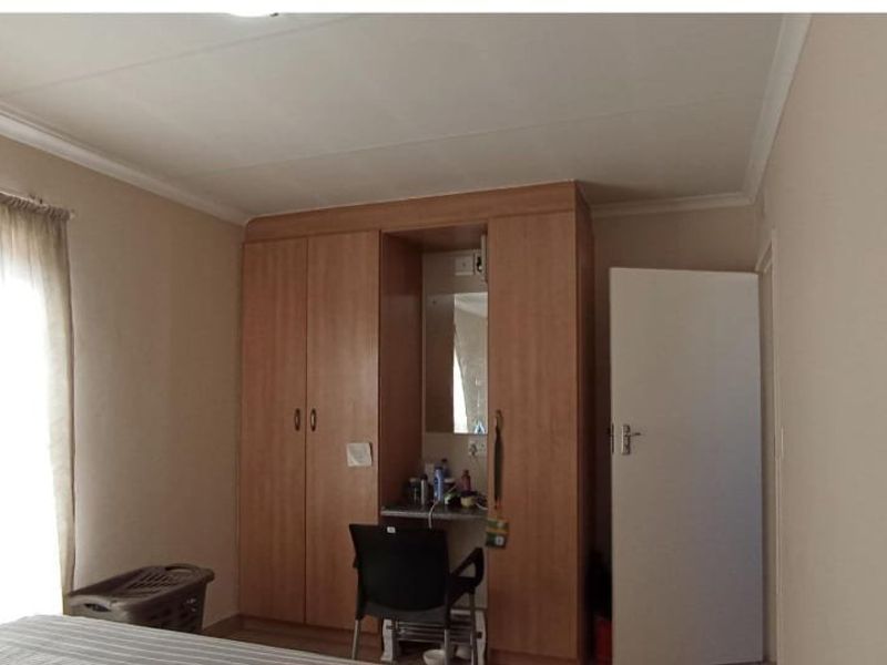 A bedroom featuring built-in wooden cupboards with an integrated vanity area and neutral wall finishes.