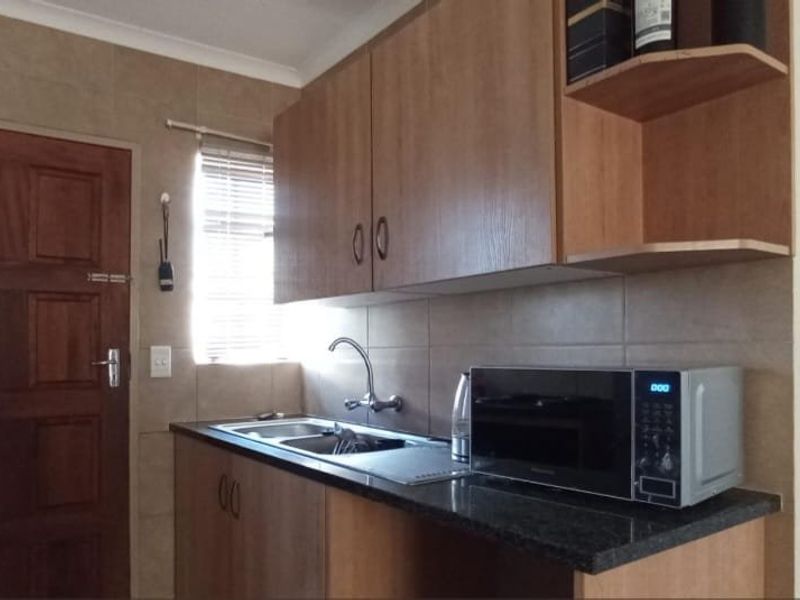 A functional kitchen featuring laminate cabinetry, granite countertops, a stainless steel sink, and tiled splashbacks, providing a practical workspace.