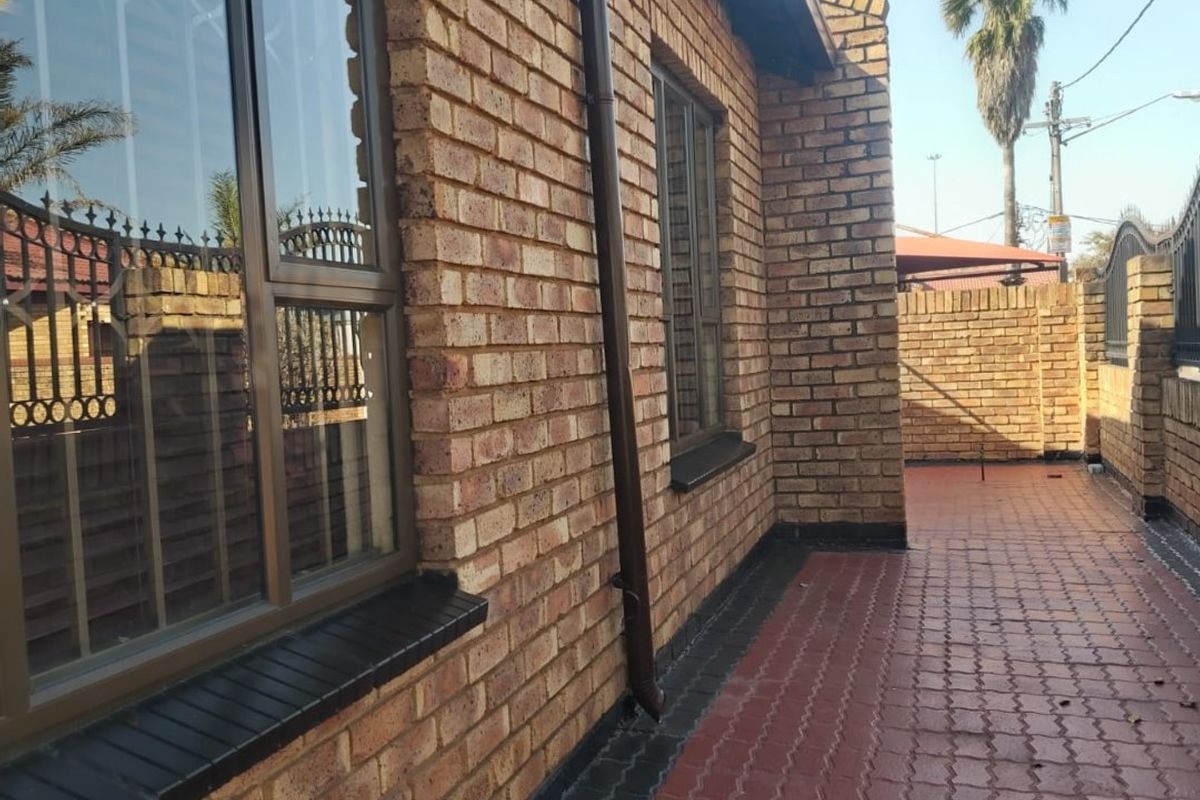 A well-maintained rear exterior view featuring face brick walls, aluminium window frames, and a clean paved walkway along the side of the house.