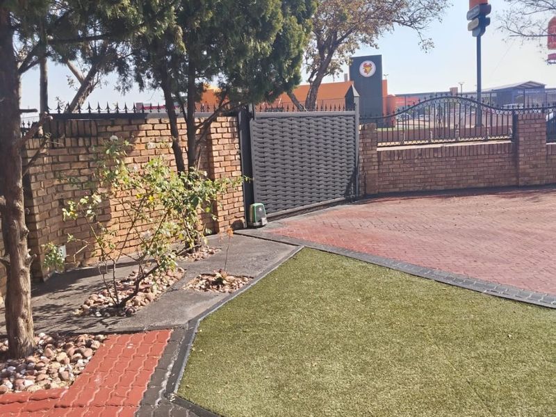 Front exterior view featuring a paved driveway, artificial lawn, brick boundary wall, and a secure sliding gate with an automated motor.