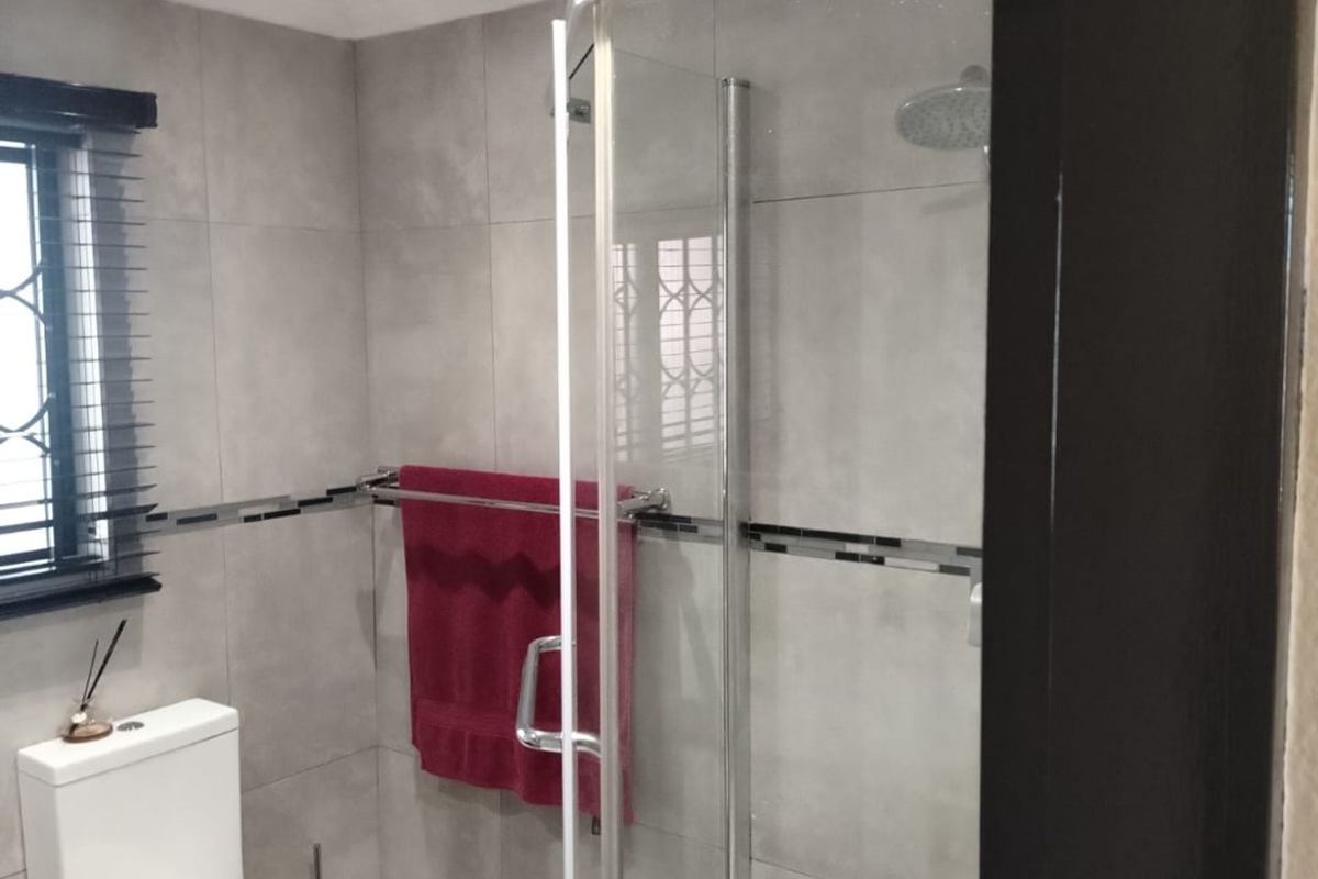 Modern bathroom featuring a glass-enclosed shower with a rain shower head, neutral grey wall tiles, and a contemporary toilet.