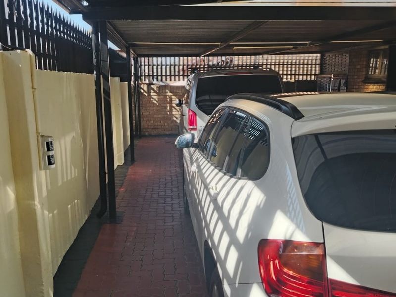 A covered carport area featuring paved flooring and perimeter walling with security spikes, providing sheltered off-street parking.