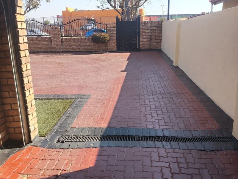 A well-maintained paved driveway and entrance area featuring a brick boundary wall, metal security gate, and integrated drainage system.
