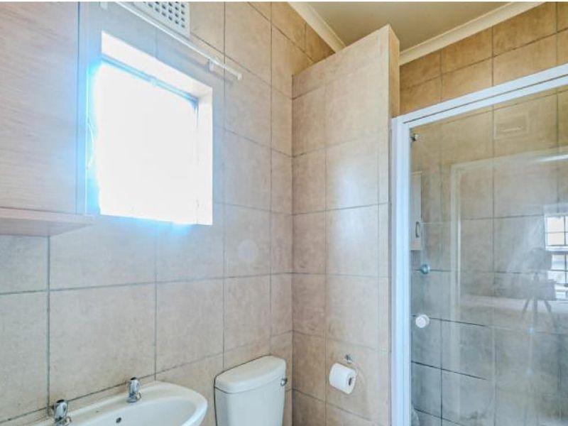A functional bathroom featuring a shower enclosure, pedestal basin, toilet, and neutral ceramic wall tiling throughout.