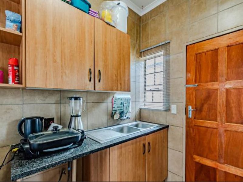 A functional scullery area featuring built-in wooden cabinetry, granite countertops, a double sink, and tiled wall finishes.