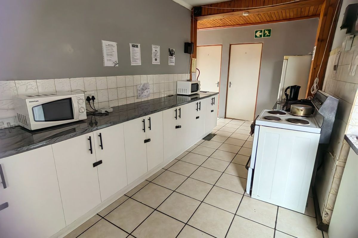 Functional kitchen featuring white cabinetry, dark laminate countertops, tiled backsplash, and ceramic flooring, with a freestanding electric stove and timber ceiling accents.