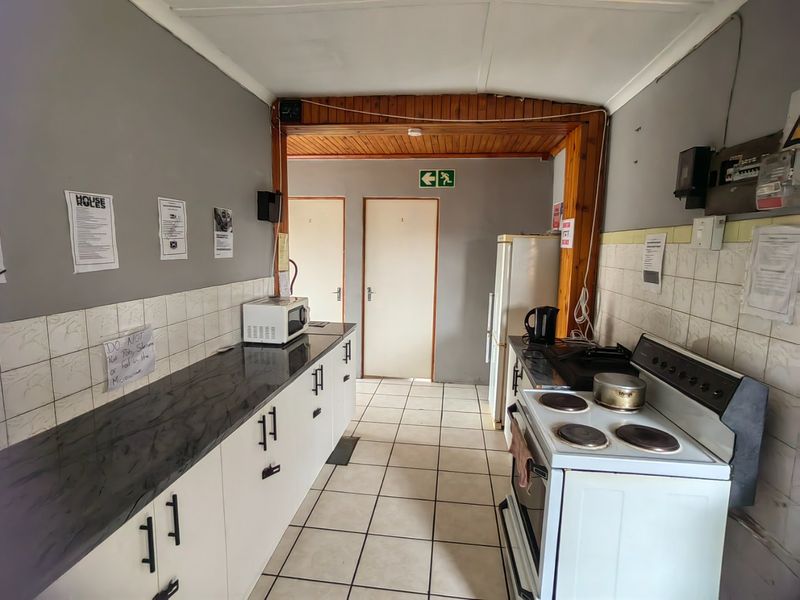 A functional kitchen featuring laminate countertops, built-in cabinetry, and a freestanding electric stove, with tiled flooring and a timber-trimmed ceiling.