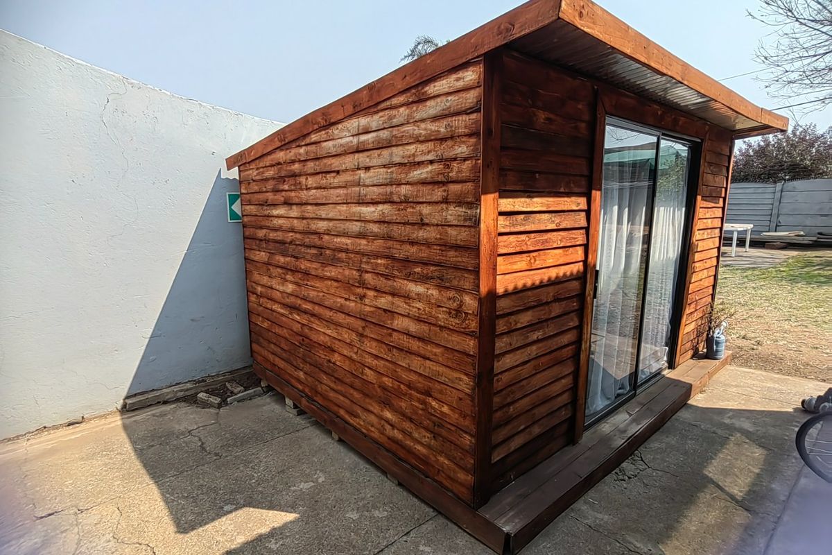 A well-maintained timber-clad garden structure featuring a sliding glass door, set on a concrete patio in the rear yard.