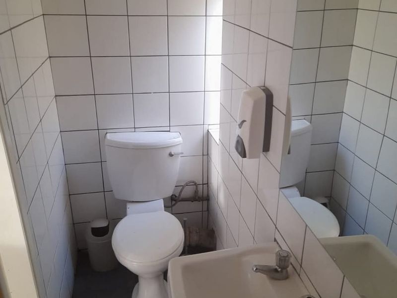 A compact bathroom featuring a white toilet, wall-mounted basin, and full-height wall tiling. The space is functional but requires cosmetic updates.