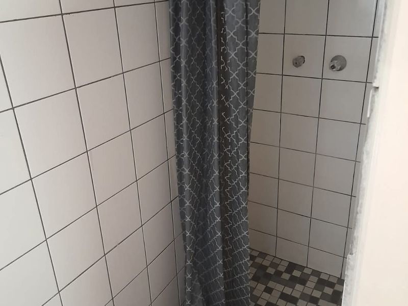 A basic shower stall featuring white wall tiles, a mosaic floor, and exposed plumbing fixtures requiring maintenance or renovation.