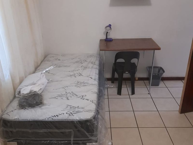 A simple bedroom featuring ceramic floor tiles and a wall-mounted shelf, providing a functional and basic living space.