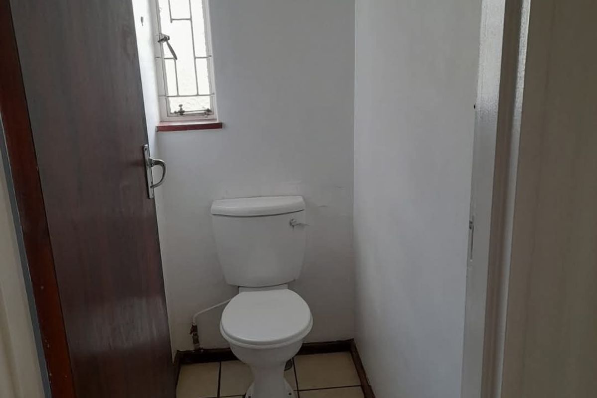 A compact, functional guest toilet featuring tiled flooring, a standard white toilet suite, and a small window with security bars.