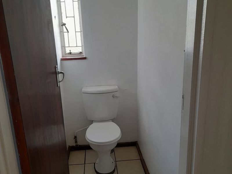 A compact, functional guest toilet featuring tiled flooring, a standard white toilet suite, and a small window with security bars.