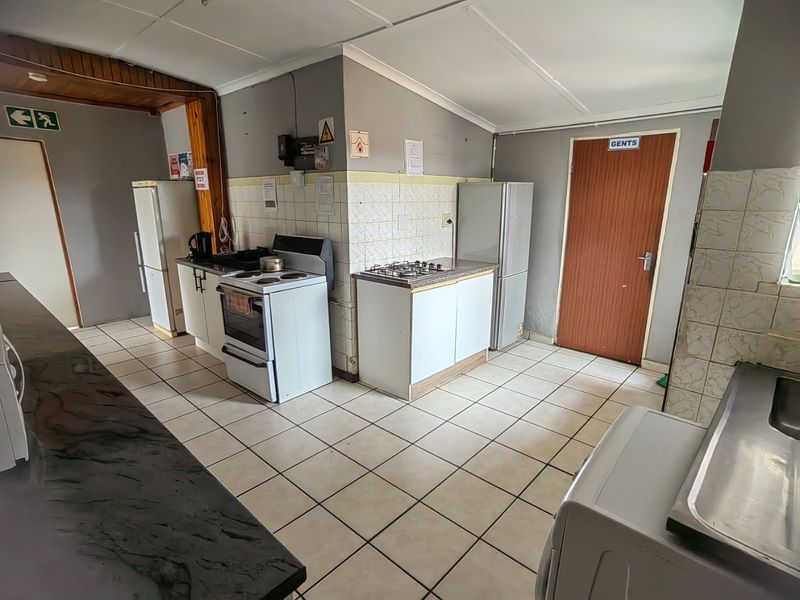 A functional kitchen area featuring tiled flooring, built-in cabinetry, a freestanding stove, and a gas hob, requiring cosmetic updates to modernize the space.